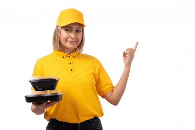 Weiblicher Kurier der Vorderansicht in der gelben Kappe des gelben Hemdes, die Schalen mit Essen auf Weiß hält