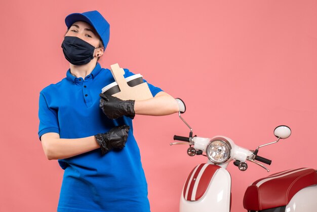 Weiblicher Kurier der Vorderansicht in der Maske mit Lieferkaffee auf dem Rosa