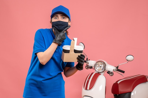 Weiblicher Kurier der Vorderansicht in der Maske mit Lieferkaffee auf dem Rosa