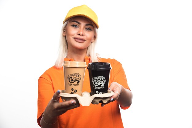 Weiblicher Kurier, der zwei Tassen Kaffee auf weißem Hintergrund beim Lächeln hält. Hochwertiges Foto