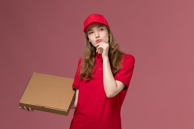 weiblicher Kurier in der roten Uniform, die das Denken der Nahrungsmittelbox auf rosa, einheitlichem Dienstlieferungsjob hält