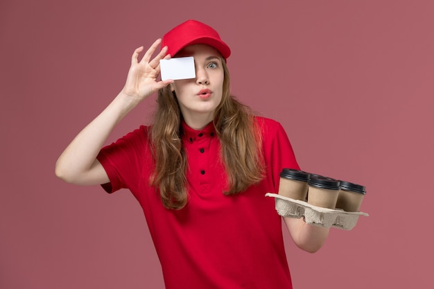 weiblicher Kurier in der roten Uniform, die Kaffeetassen mit Karte aufwirbelt, die auf rosa, einheitlicher Dienst, der Arbeiter liefert, aufwirft
