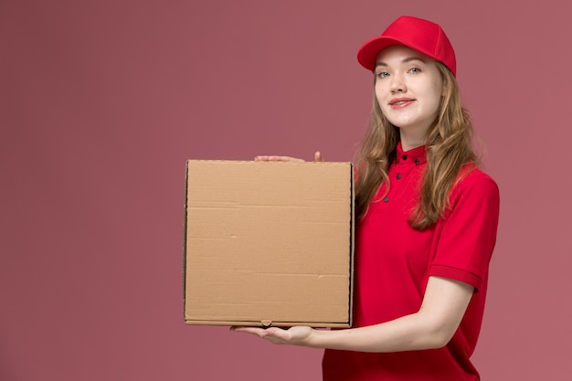 weiblicher Kurier in der roten Uniform, die Nahrungsmittellieferbox auf rosa, einheitlichem Dienstlieferungsarbeitsjob hält