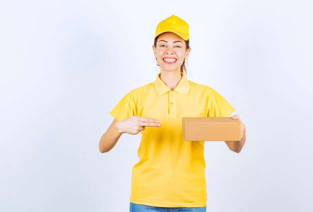 Weiblicher Kurier in gelber Uniform, der ein Papppaket liefert und sich positiv fühlt.
