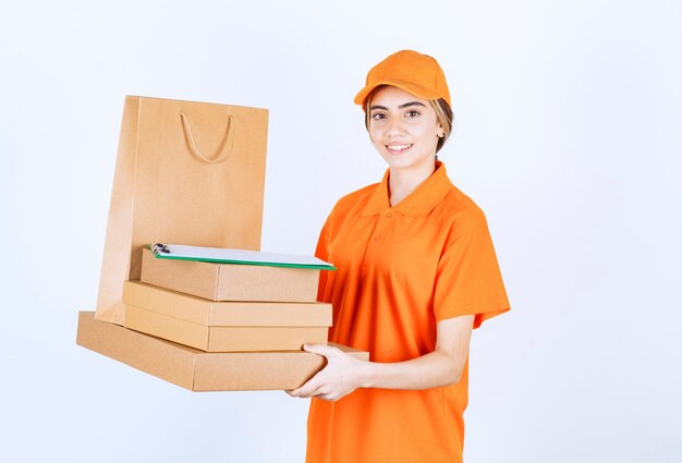 Weiblicher Kurier in orangefarbener Uniform mit einem Vorrat an Papppaketen und Einkaufstüten