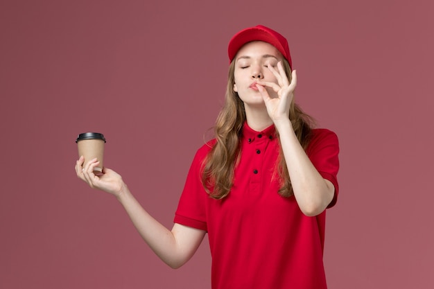 Weiblicher kurier in roter uniform, die kaffeetasse auf dem rosa, einheitlichen dienstlieferungsjobarbeiter hält