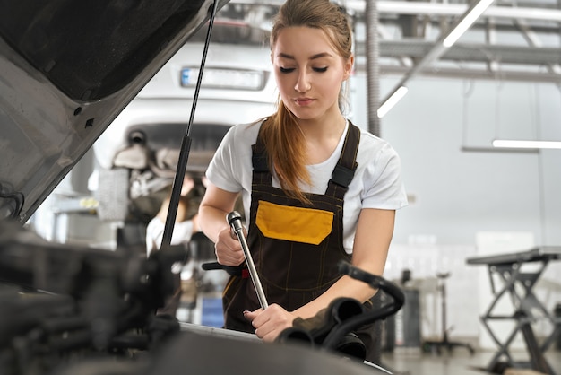 Kostenloses Foto weiblicher mechaniker, der automobil unter motorhaube befestigt.