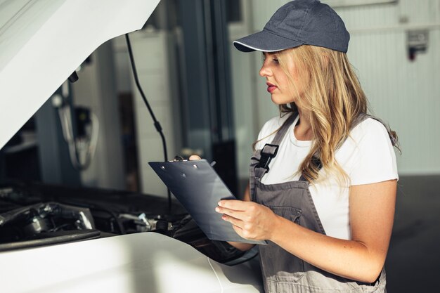 Weiblicher Mechaniker der Vorderansicht, der Auto kontrolliert