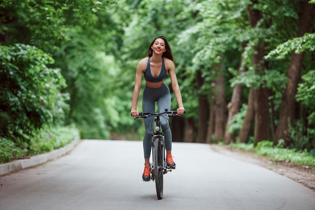 Weiblicher Radfahrer auf einem Fahrrad auf Asphaltstraße im Wald am Tag