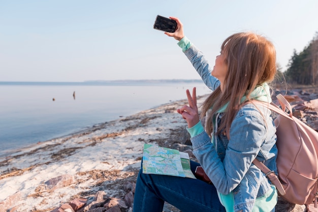 Weiblicher Reisender, der auf dem Strand nimmt selfie am Handy sitzt