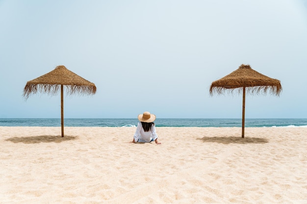 Weiblicher Reisender, der auf Sand nahe Ozean sitzt