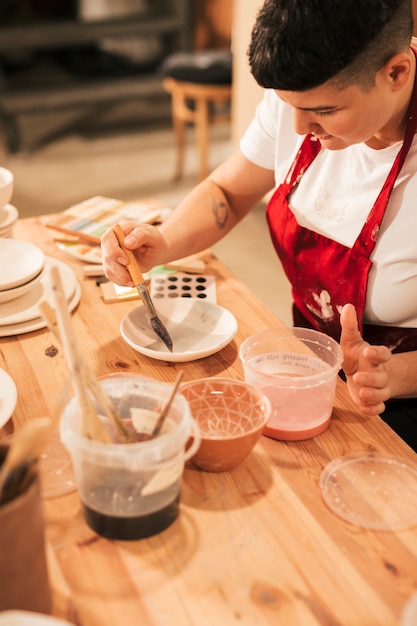 Weiblicher Töpfer, der keramischen Dishware mit Malerpinsel in der Werkstatt malt