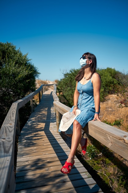 Weiblicher Tourist in einer Wegwerfmaske, die auf der Brücke sitzt
