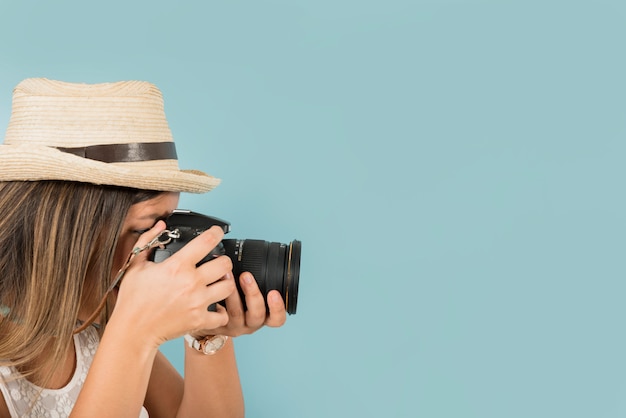 Weiblicher Tourist macht ein Foto mit Berufskamera gegen blauen Hintergrund