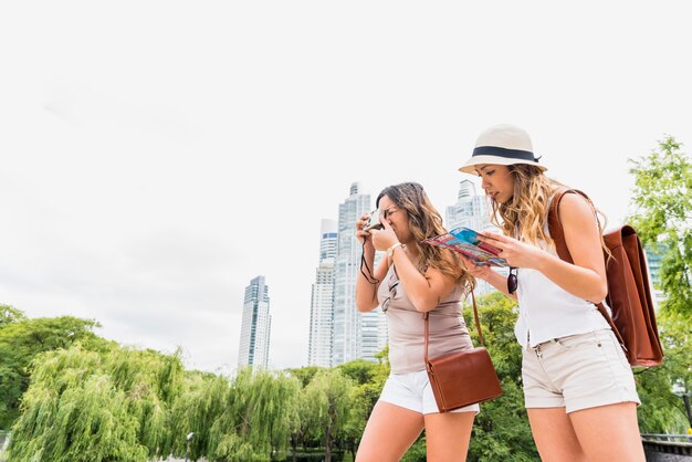Weiblicher Tourist zwei, der Foto von der Kamera und von ihrem Freund betrachtet Karte macht