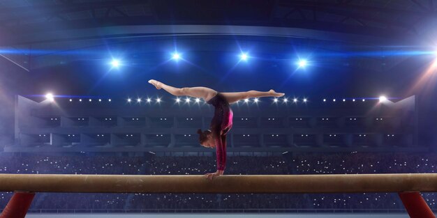 Weiblicher Turner, der einen komplizierten Trick auf dem Schwebebalken der Gymnastik in einer professionellen Arena macht