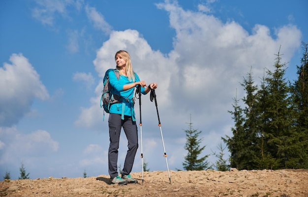 Weiblicher Wanderer, der auf Bergstraße gegen blauen bewölkten Himmel steht