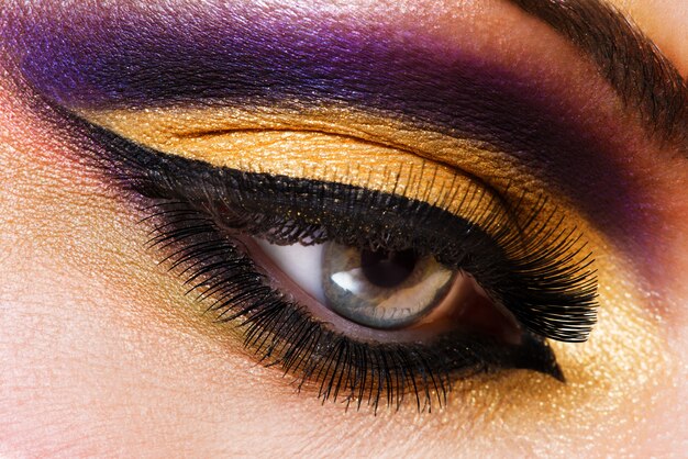 Weibliches Auge der Nahaufnahme mit dem hellen Make-up der schönen Mode
