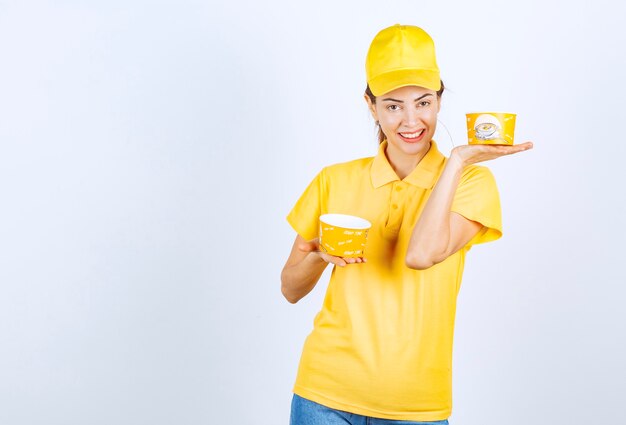Weibliches Mädchen in gelber Uniform, die zwei Nudelschalen zum Mitnehmen hält.