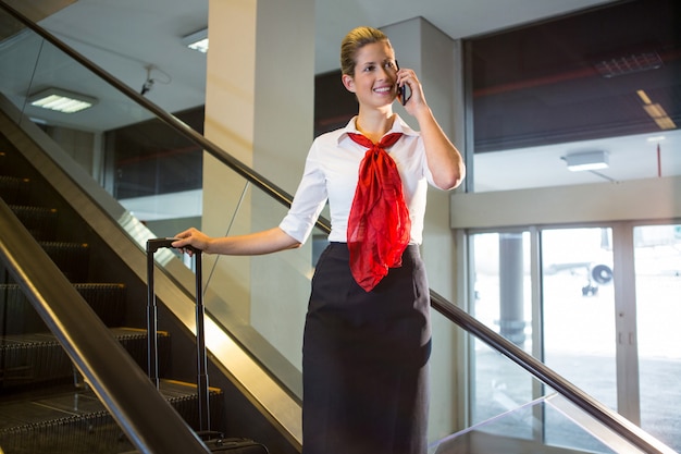 Weibliches Personal mit Gepäck, das auf Mobiltelefon auf Rolltreppe spricht