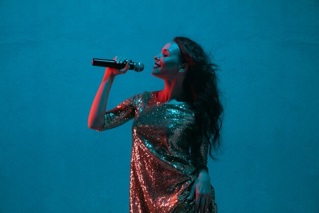 Weibliches Sängerporträt lokalisiert auf blauer Studiowand im Neonlicht