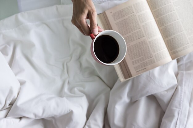 Weiche Foto von Frau auf dem Bett mit alten Buch und Tasse Kaffee und Kopie Raum.