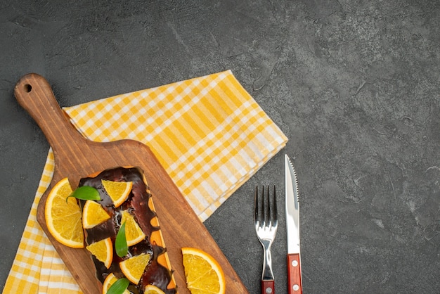 Weiche Kuchen an Bord und Zitronen mit Blättern auf grün gestreiftem Handtuch des dunklen Tisches schneiden