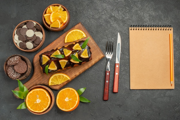 Weiche kuchen auf holzschneidebrett und orangen mit blattkeksen und notizbuch schneiden