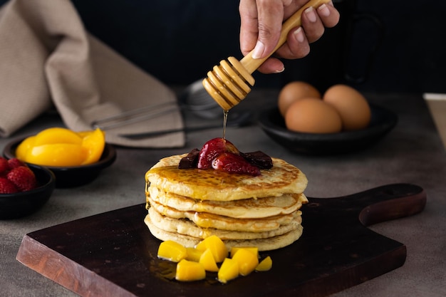 Weicher Fokus eines Stapels flauschiger Pfannkuchen mit frischen Früchten und Honig auf einem Holzbrett