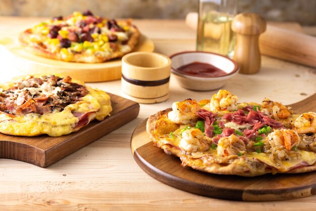 Weicher Fokus hausgemachter traditioneller Pizzen mit verschiedenen Belägen auf einem Holztisch