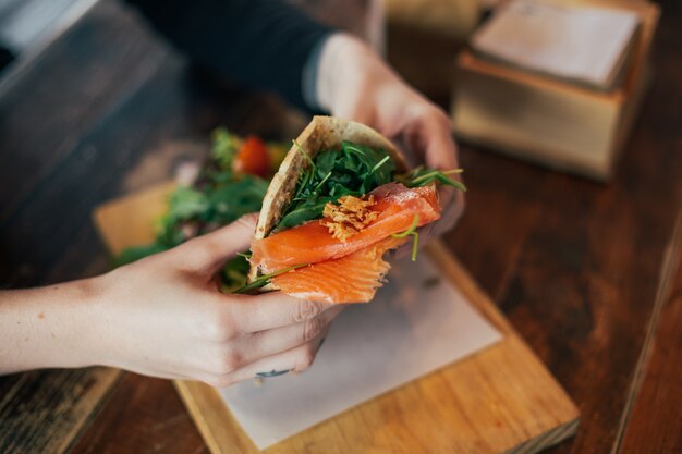 Weichzeichneraufnahme des Mannes, der köstliches großes Frühstück im kühlen Restaurant oder im Café hat, setzt Guacamole oder Avocado auf Roggenbrot-Toast