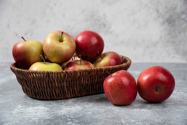 Weidenkorb mit roten saftigen Äpfeln auf Marmoroberfläche.