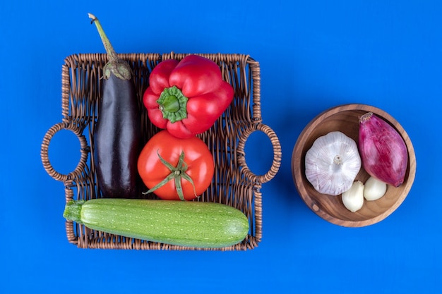 Weidenkorb und Schüssel mit frischem Gemüse auf blauem Untergrund.