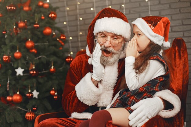Weihnachten, Kind und Geschenke. Der Weihnachtsmann brachte dem Kind Geschenke. Freudiges kleines Mädchen, das den Weihnachtsmann umarmt.