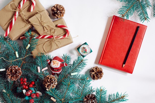 Weihnachts- oder Neujahrshintergrund: Fichte, Zweige, Geschenke, Dekoration, rotes Notizbuch mit Stift auf weißem Hintergrund