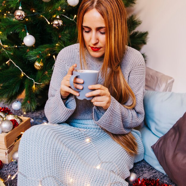 Weihnachts- und Teekonzept mit der Frau, die Becher betrachtet