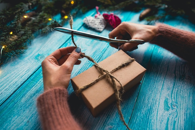 Kostenloses Foto weihnachtsartikel auf einem blauen holztisch. die hände der frau, die weihnachtsgeschenk einwickeln.