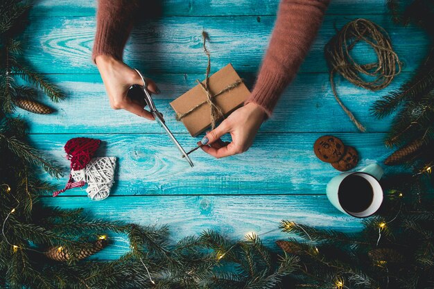 Weihnachtsartikel auf einem blauen wodden Tisch. Die Hände der Frau, die Weihnachtsgeschenk einwickeln.