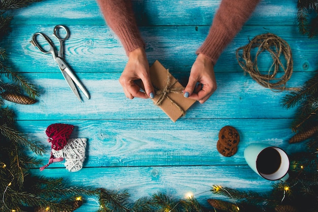 Weihnachtsartikel auf einem blauen wodden Tisch. Die Hände der Frau, die Weihnachtsgeschenk einwickeln.