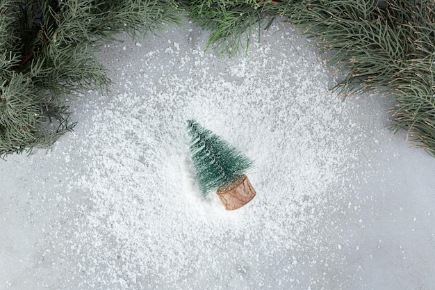Weihnachtsbaumfigur neben einem immergrünen Ast auf Marmortisch.