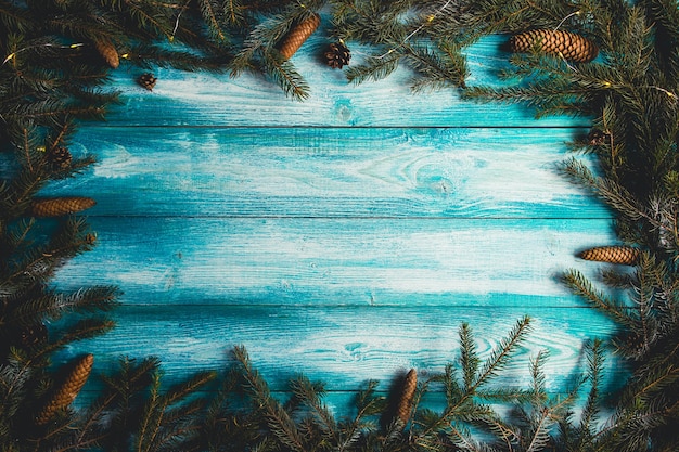 Weihnachtsblauer hölzerner Hintergrund mit Tannenzweigen und Weihnachtslichtern.