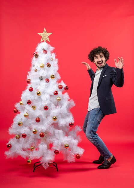 Weihnachtsfeier mit glücklichem lustigem aufgeregtem jungen Mann, der nahe Weihnachtsbaum tanzt