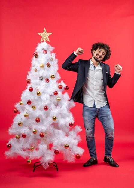 Weihnachtsfeier mit jungen glücklichen aufgeregten lustigen Manntanzen, das nahe Weihnachtsbaum steht