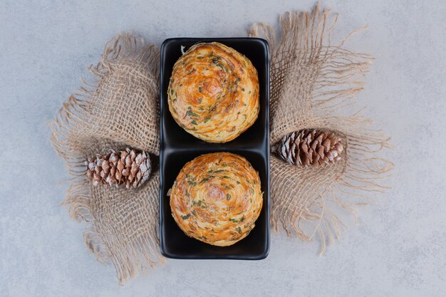 Weihnachtsgebäck auf schwarzem Teller mit Tannenzapfen.