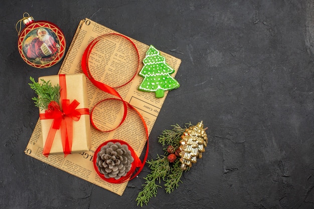 Weihnachtsgeschenk von oben in braunem Papierzweigtannenband auf Zeitungsweihnachtsverzierungen auf dunkler Oberfläche