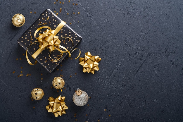 Weihnachtsgeschenkbox oder geschenk mit band, goldenem konfetti und goldenen kugeln auf schwarzem hintergrund. magische weihnachtsgrußkarte. weihnachtsdekoration. grenzdesign. attrappe, lehrmodell, simulation. ansicht von oben.