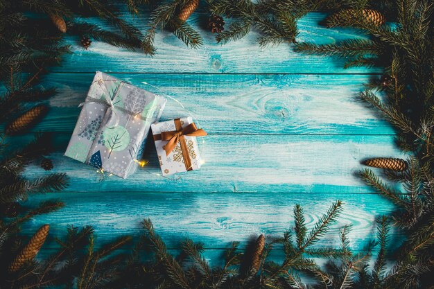 Weihnachtsgeschenke auf blauem Holztisch mit Tannenzweigen und Weihnachtslichtern.