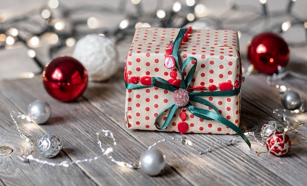 Weihnachtshintergrund mit Geschenkbox hautnah auf Holzoberfläche, Weihnachtskugeln und Bokeh-Lichtern.