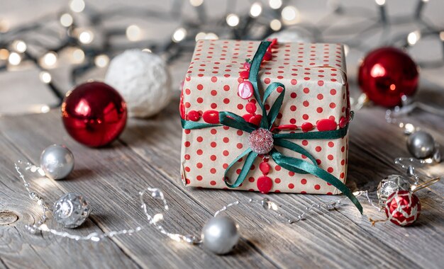 Weihnachtshintergrund mit Geschenkbox hautnah auf Holzoberfläche, Weihnachtskugeln und Bokeh-Lichtern.