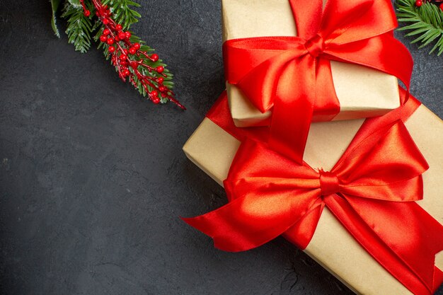 Weihnachtshintergrund mit schönen Geschenken mit bogenförmigem Band und Tannenzweigen auf einem dunklen Tisch
